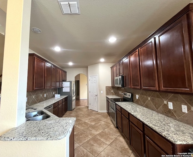 kitchen featuring light stone counters, sink, kitchen peninsula, backsplash, and stainless steel appliances