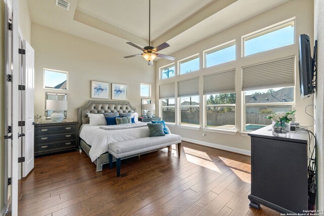 bedroom with ceiling fan, a tray ceiling, dark hardwood / wood-style flooring, and a high ceiling