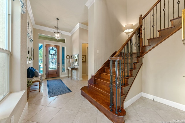 foyer featuring light tile patterned flooring, a chandelier, ornamental molding, and a high ceiling