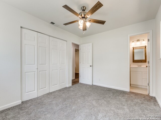 unfurnished bedroom featuring a closet, light colored carpet, ceiling fan, and ensuite bath