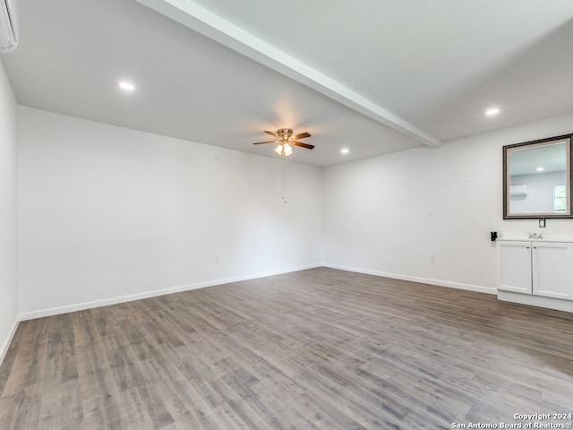 empty room featuring ceiling fan, a wall unit AC, wood-type flooring, and beamed ceiling