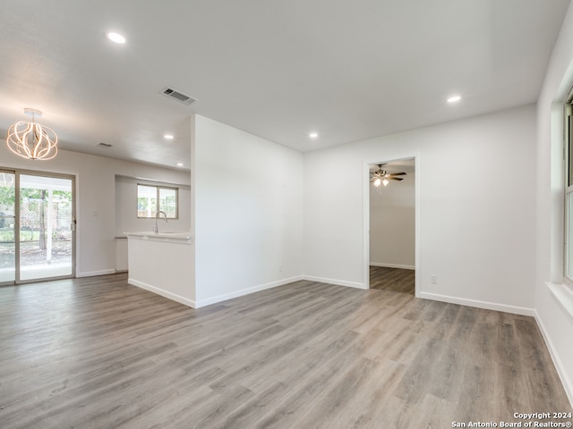 empty room with sink, ceiling fan with notable chandelier, and light hardwood / wood-style flooring