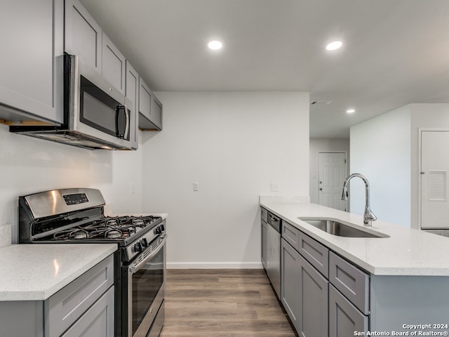 kitchen with stainless steel appliances, wood-type flooring, kitchen peninsula, sink, and gray cabinets