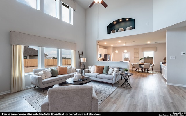 living room featuring ceiling fan, light hardwood / wood-style flooring, a high ceiling, and a wealth of natural light