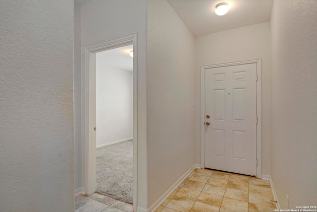 entryway featuring light tile patterned floors, a textured wall, and baseboards