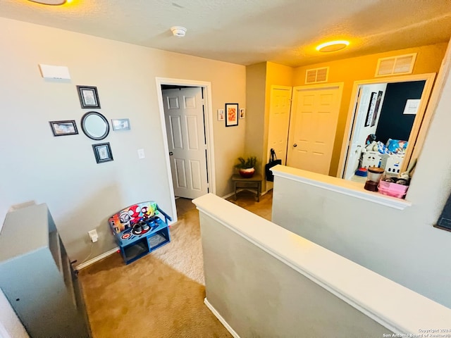 hallway with a textured ceiling and light carpet