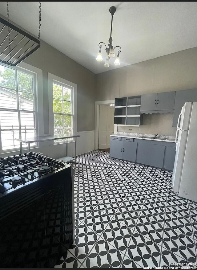 kitchen with white refrigerator, black range oven, a chandelier, and gray cabinetry