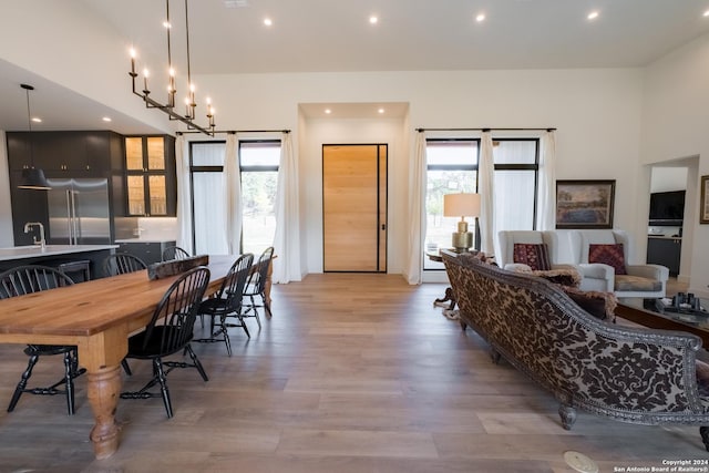 dining area with light wood-type flooring, a high ceiling, a wealth of natural light, and an inviting chandelier