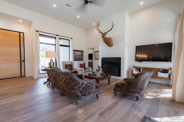 living room featuring ceiling fan, light hardwood / wood-style flooring, and a high ceiling