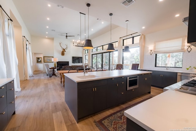 kitchen featuring a kitchen island with sink, sink, hanging light fixtures, light hardwood / wood-style flooring, and a healthy amount of sunlight