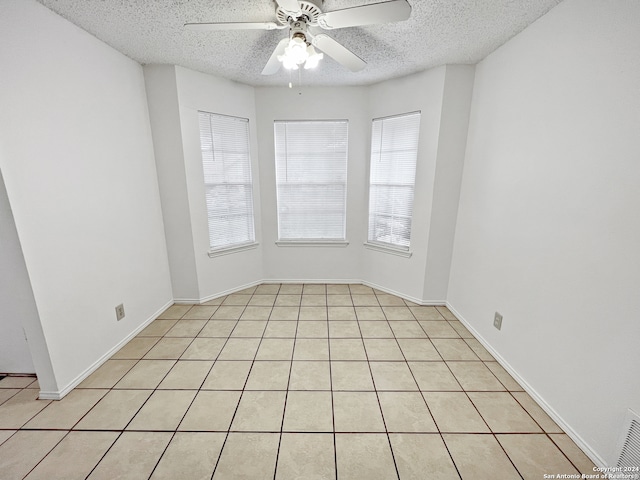 empty room featuring a textured ceiling, light tile patterned floors, and ceiling fan