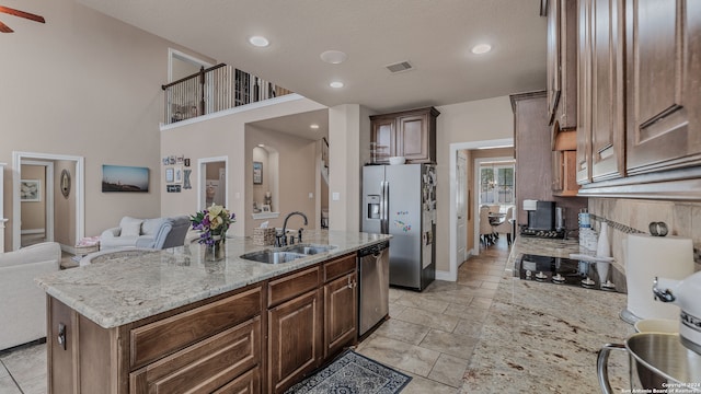 kitchen with ceiling fan, light stone counters, sink, a center island with sink, and appliances with stainless steel finishes