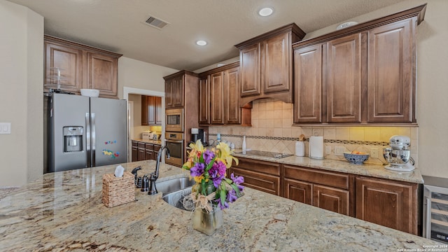 kitchen featuring wine cooler, light stone counters, sink, backsplash, and appliances with stainless steel finishes