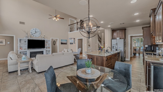 dining space with ceiling fan with notable chandelier, a towering ceiling, beverage cooler, and sink