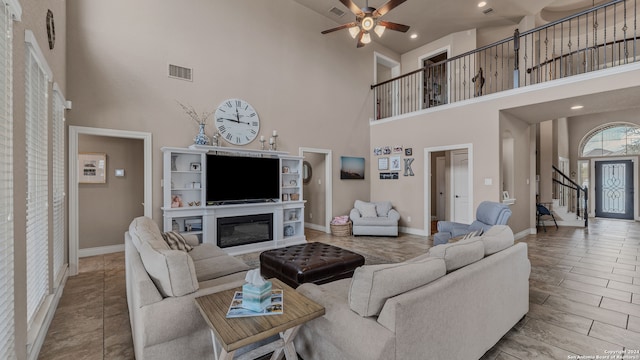 living room with ceiling fan, a towering ceiling, and light hardwood / wood-style floors