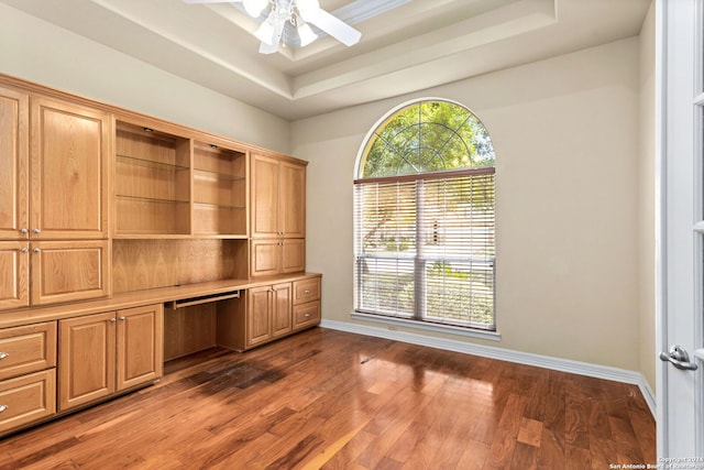 unfurnished office featuring built in desk, ceiling fan, a raised ceiling, and dark hardwood / wood-style flooring