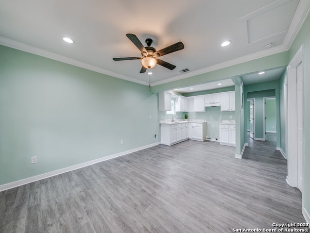 unfurnished living room featuring ceiling fan, sink, light wood-type flooring, and ornamental molding