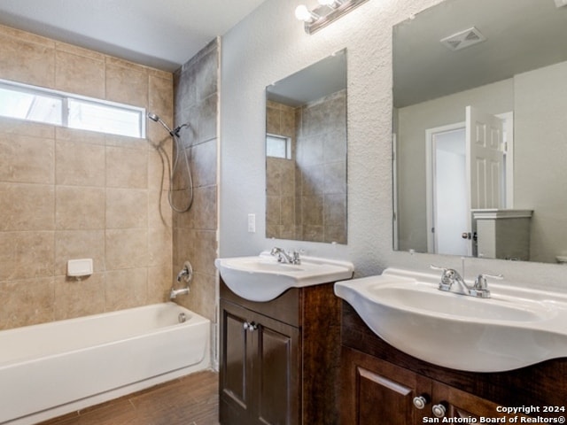 bathroom featuring wood-type flooring, tiled shower / bath combo, and vanity