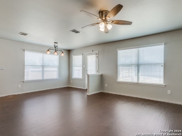 empty room with ceiling fan with notable chandelier and dark hardwood / wood-style floors