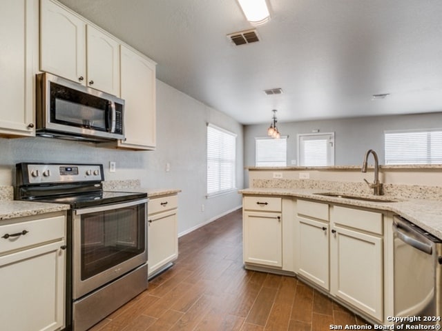 kitchen featuring pendant lighting, sink, cream cabinets, dark wood-type flooring, and appliances with stainless steel finishes