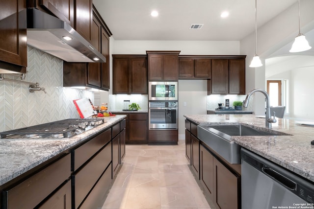 kitchen featuring wall chimney range hood, decorative light fixtures, decorative backsplash, light stone countertops, and appliances with stainless steel finishes