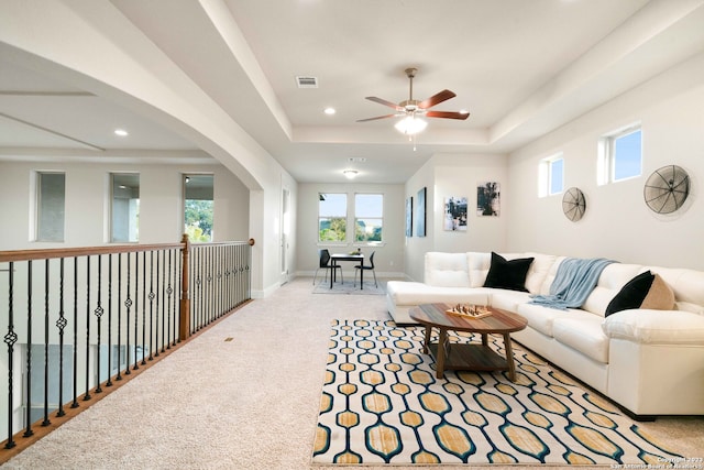 living room with a tray ceiling, light colored carpet, and ceiling fan