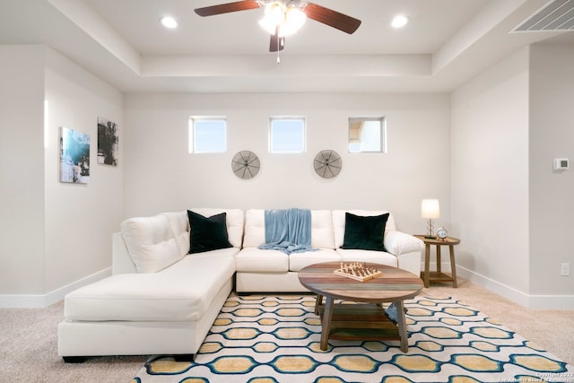 carpeted living room with ceiling fan and a tray ceiling