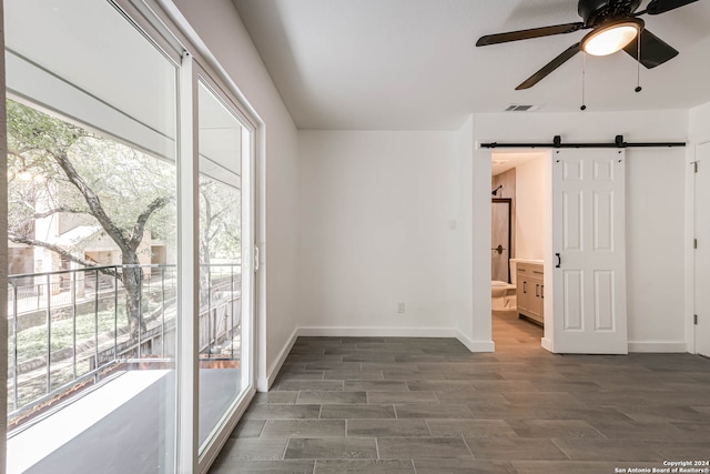 empty room featuring ceiling fan, dark hardwood / wood-style floors, and a barn door