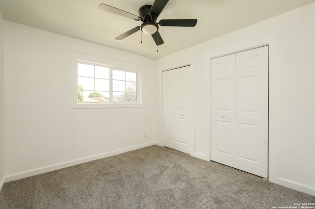 unfurnished bedroom with two closets, light carpet, and ceiling fan