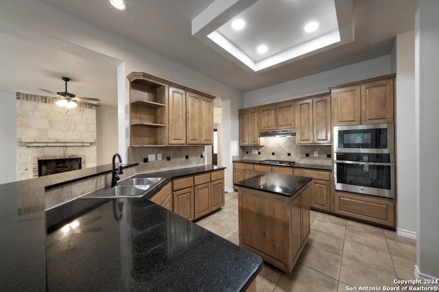 kitchen with a center island, sink, decorative backsplash, a stone fireplace, and ceiling fan