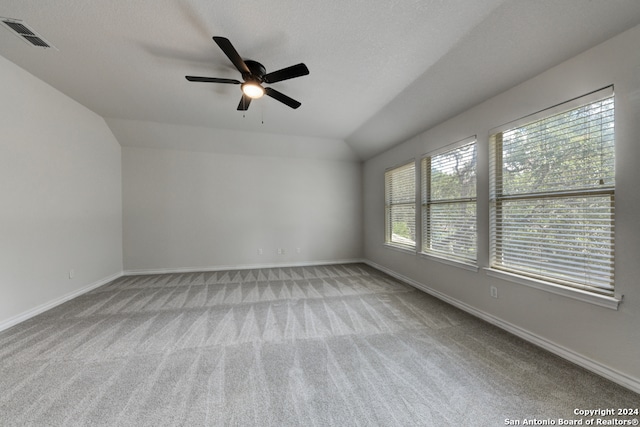 empty room with a textured ceiling, vaulted ceiling, light carpet, and ceiling fan