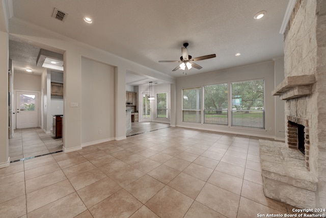 unfurnished living room with light tile patterned floors, ceiling fan, a fireplace, and a textured ceiling