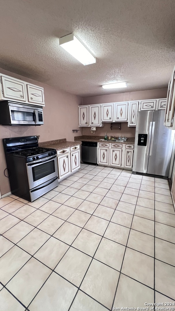 kitchen with white cabinets, a textured ceiling, appliances with stainless steel finishes, and light tile patterned floors