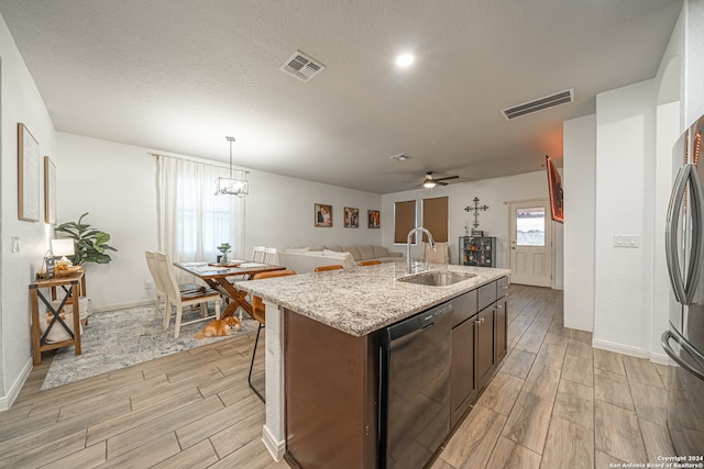 kitchen with dark brown cabinetry, an island with sink, sink, black dishwasher, and ceiling fan with notable chandelier