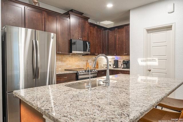 kitchen with appliances with stainless steel finishes, a breakfast bar, backsplash, light stone countertops, and a center island