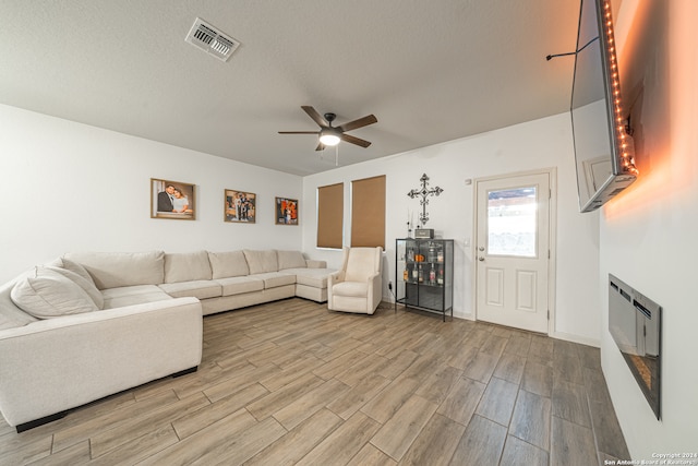 living room with light wood-type flooring, ceiling fan, a fireplace, and a textured ceiling