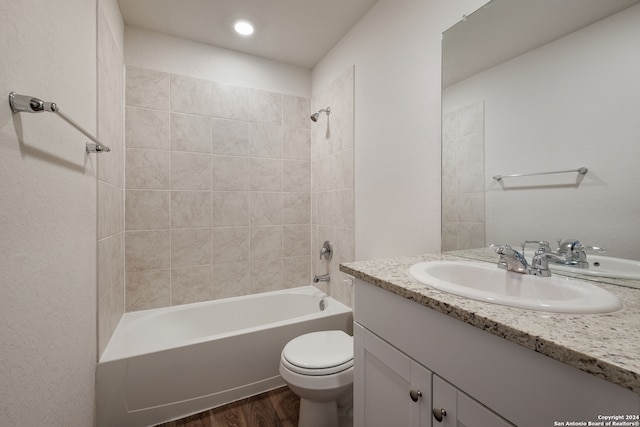 full bathroom with wood-type flooring, tiled shower / bath, vanity, and toilet