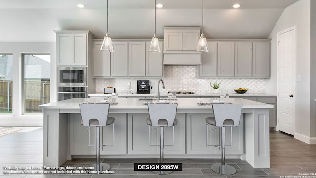 kitchen featuring appliances with stainless steel finishes, a kitchen island with sink, hanging light fixtures, and vaulted ceiling