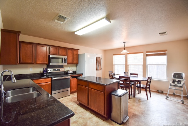 kitchen with appliances with stainless steel finishes, a kitchen island, a textured ceiling, decorative light fixtures, and sink