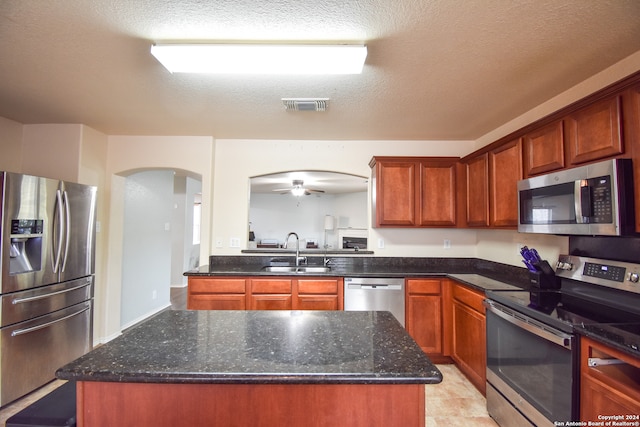 kitchen with appliances with stainless steel finishes, a kitchen island, sink, and ceiling fan