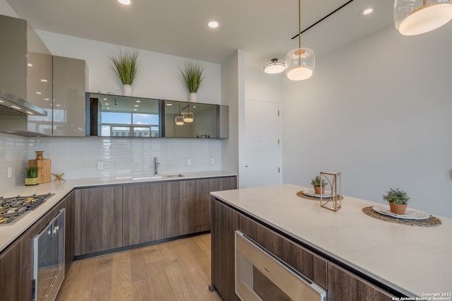 kitchen with light wood-type flooring, sink, stainless steel gas cooktop, decorative light fixtures, and light stone countertops