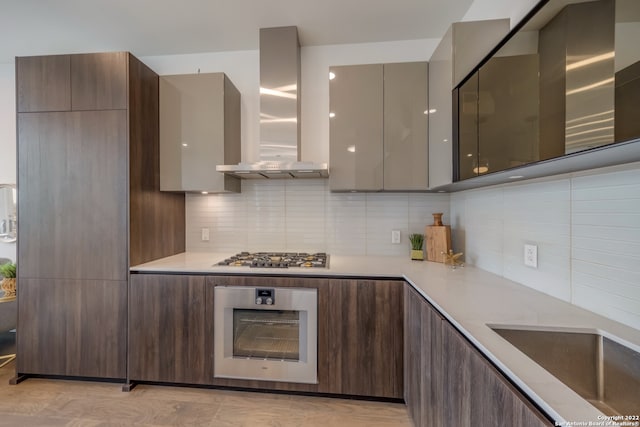 kitchen with backsplash, stainless steel appliances, dark brown cabinetry, sink, and wall chimney range hood