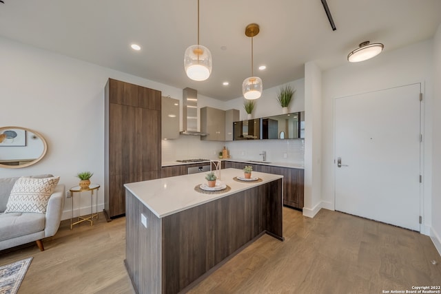 kitchen featuring pendant lighting, sink, wall chimney exhaust hood, and light hardwood / wood-style floors