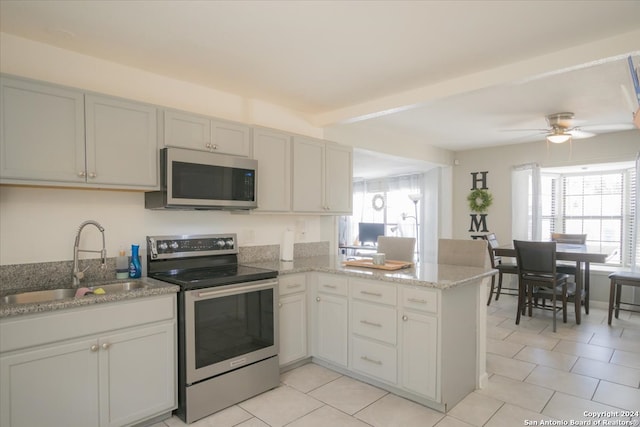 kitchen featuring appliances with stainless steel finishes, light stone counters, kitchen peninsula, ceiling fan, and sink