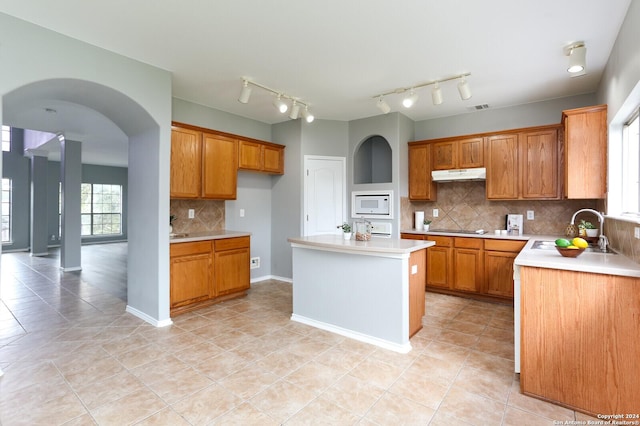 kitchen featuring sink, a kitchen island, light tile patterned flooring, backsplash, and white microwave