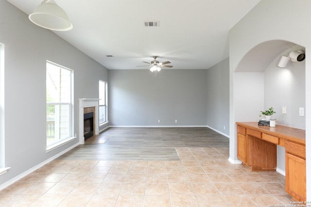 unfurnished living room with ceiling fan, a fireplace, light tile patterned floors, and a healthy amount of sunlight