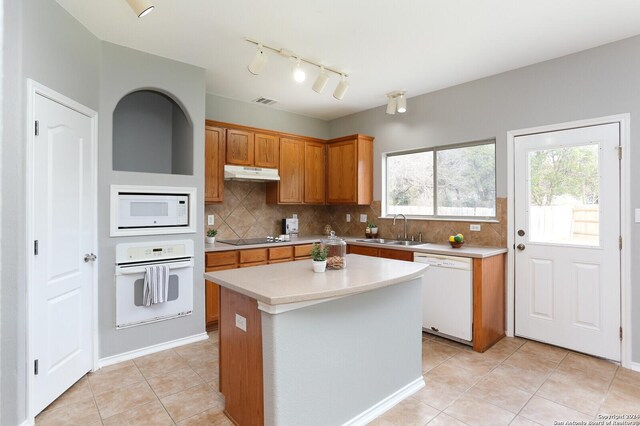 kitchen with tasteful backsplash, white appliances, sink, light tile patterned floors, and a center island