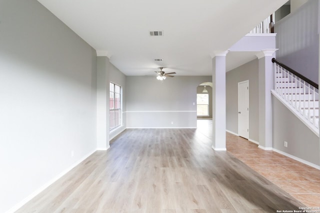 empty room with ornate columns, a wealth of natural light, light hardwood / wood-style flooring, and ceiling fan