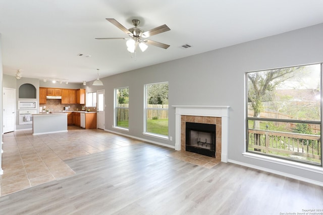 unfurnished living room featuring a tile fireplace, ceiling fan, and light hardwood / wood-style flooring