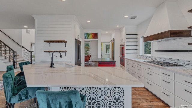 kitchen with premium range hood, sink, light hardwood / wood-style flooring, appliances with stainless steel finishes, and a kitchen bar